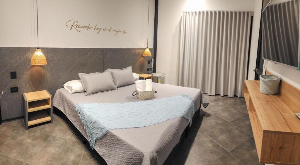 Una habitación de hotel moderna con una cama grande, mesitas de noche, un banco de madera y un televisor de pared.
