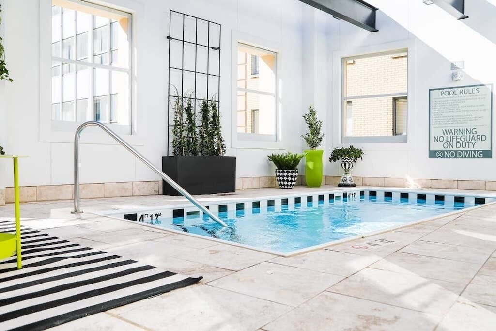 Ein Hallenbad mit Schild, das die Poolregeln erklärt, einem Rettungsschwimmerstuhl und Kübelpflanzen rund um den Pool.