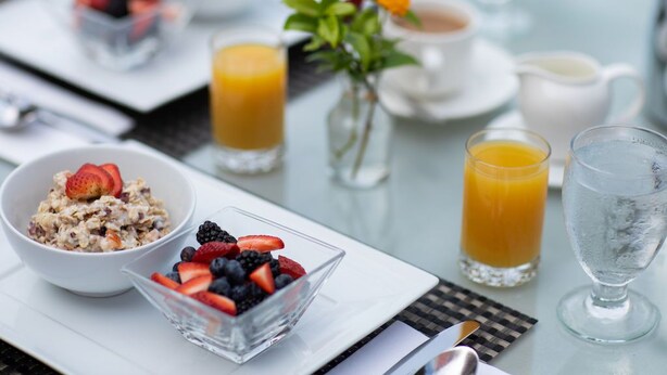 A breakfast setting with a bowl of oatmeal, a glass of orange juice, and a glass of water on a table. - Luxe 2 Bedroom Suite in Beachfront Resort (Sandys Parish)