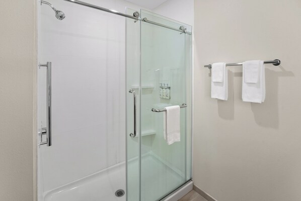 A glass-enclosed shower with a glass door, a towel rack with two white towels, and a small shelf with toiletries.