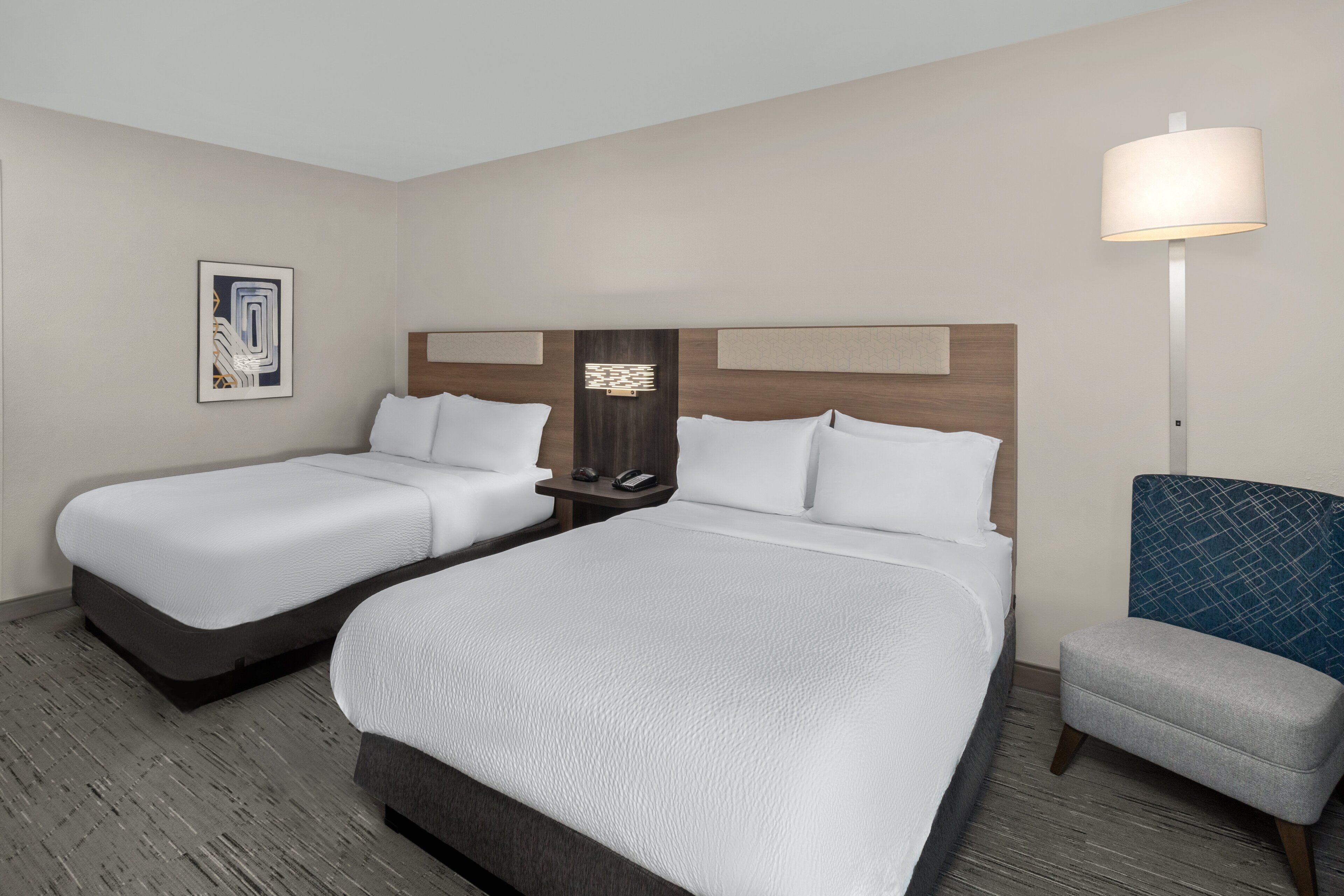 A hotel room with two beds, a desk, a chair, and a lamp.