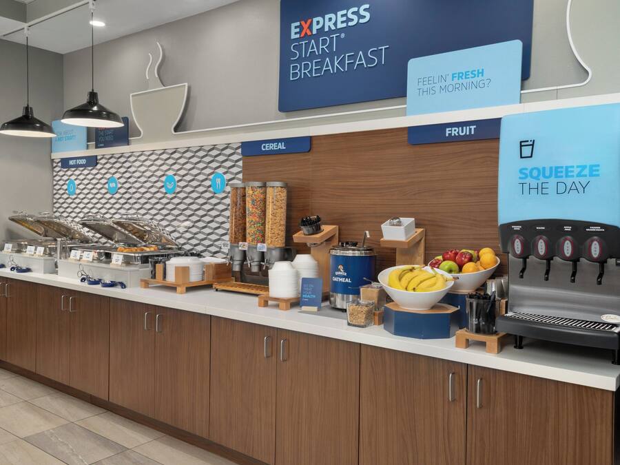 A breakfast bar with labeled sections for cereal, fruit, and hot food, and a beverage dispenser.