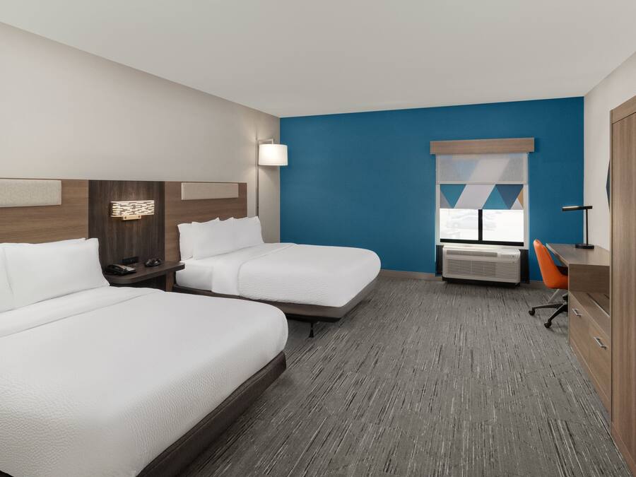 Une chambre d’hôtel avec deux lits, un bureau, une chaise, une armoire et une fenêtre avec des stores.