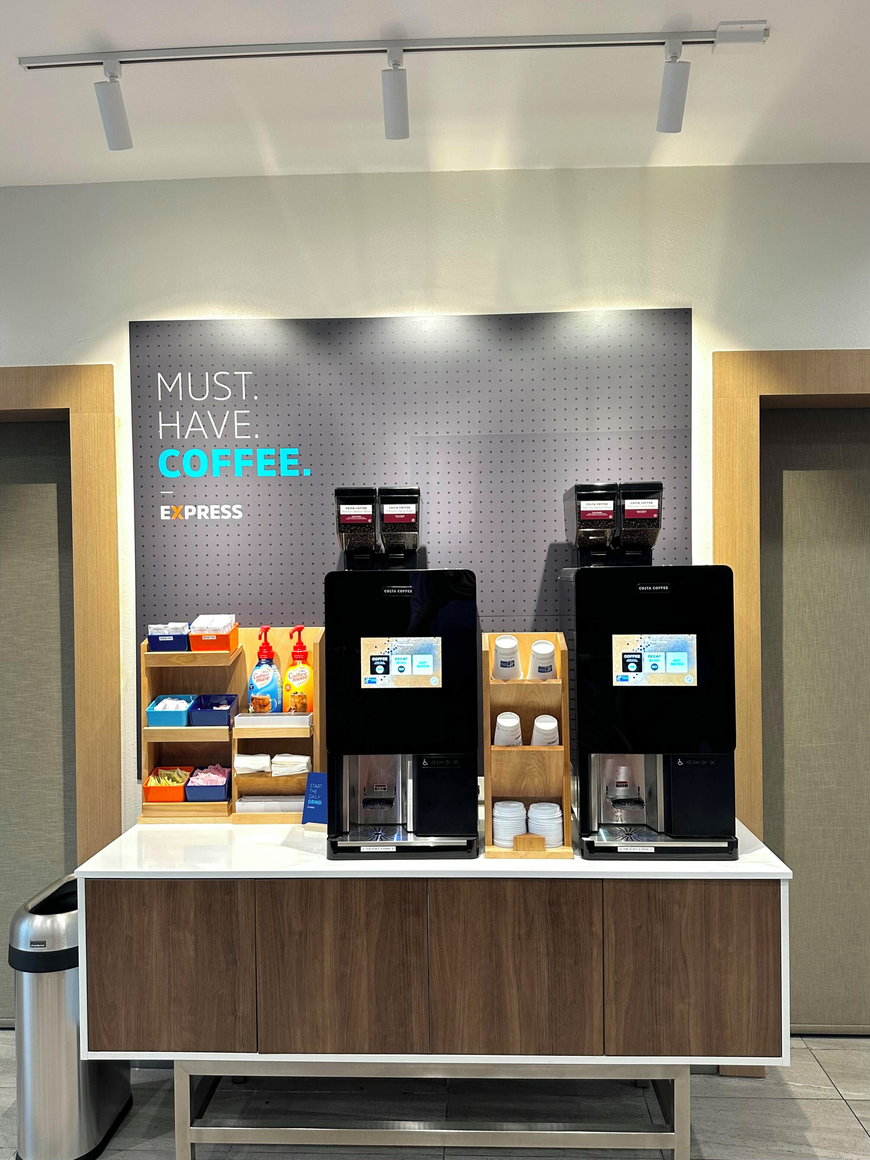 A coffee station with two espresso machines, a sign reading "MUST HAVE COFFEE", and various coffee pods and cups.