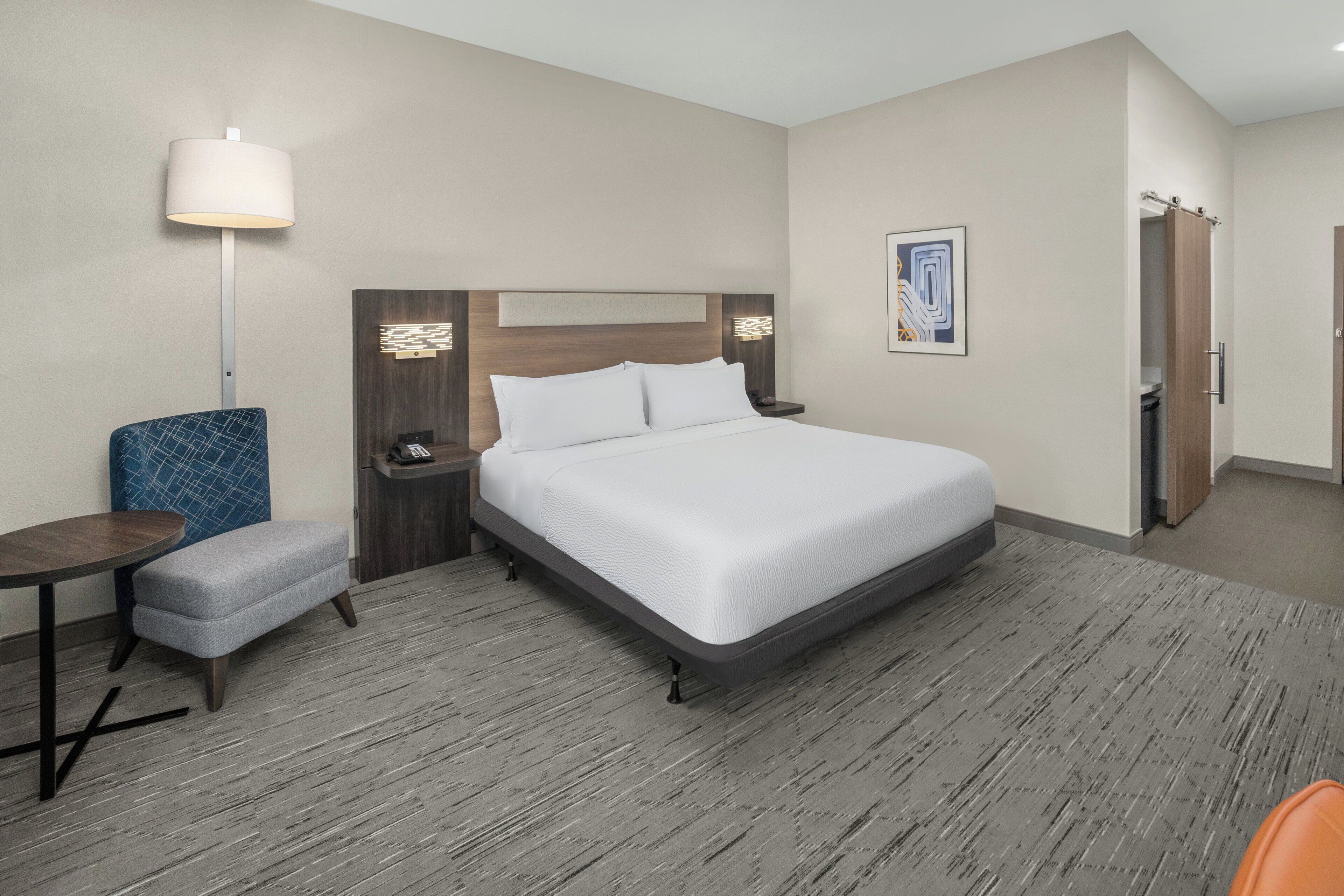 A hotel room with a large bed, a desk, a chair, and a nightstand.