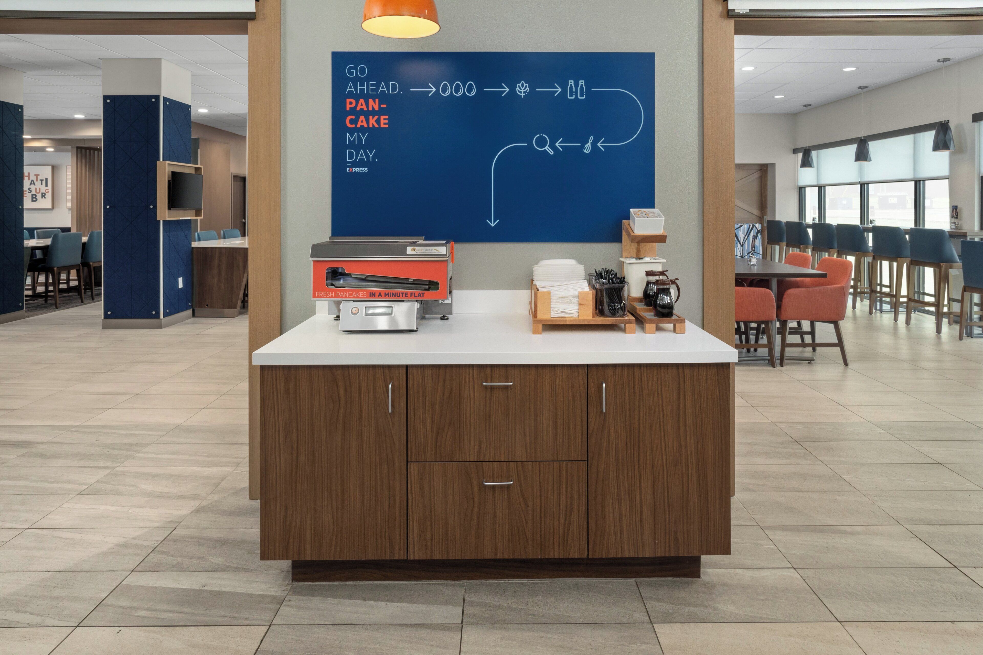 A modern kitchen area with a flat-screen TV, a coffee machine, and a chalkboard with a menu.