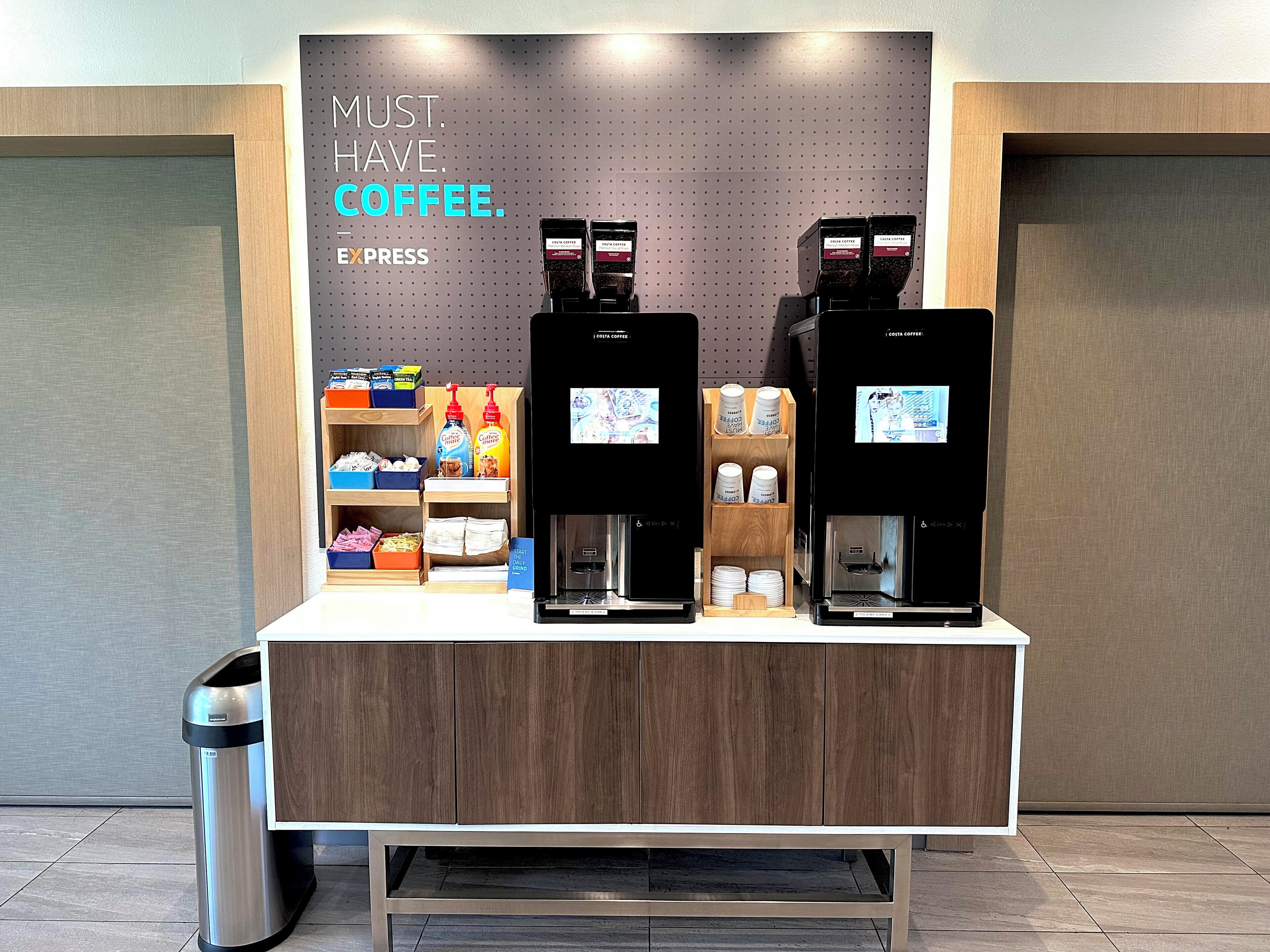 Una estación de café con dos máquinas de espresso, una exhibición de productos de café y un letrero que dice 'MUST HAVE COFFEE'.