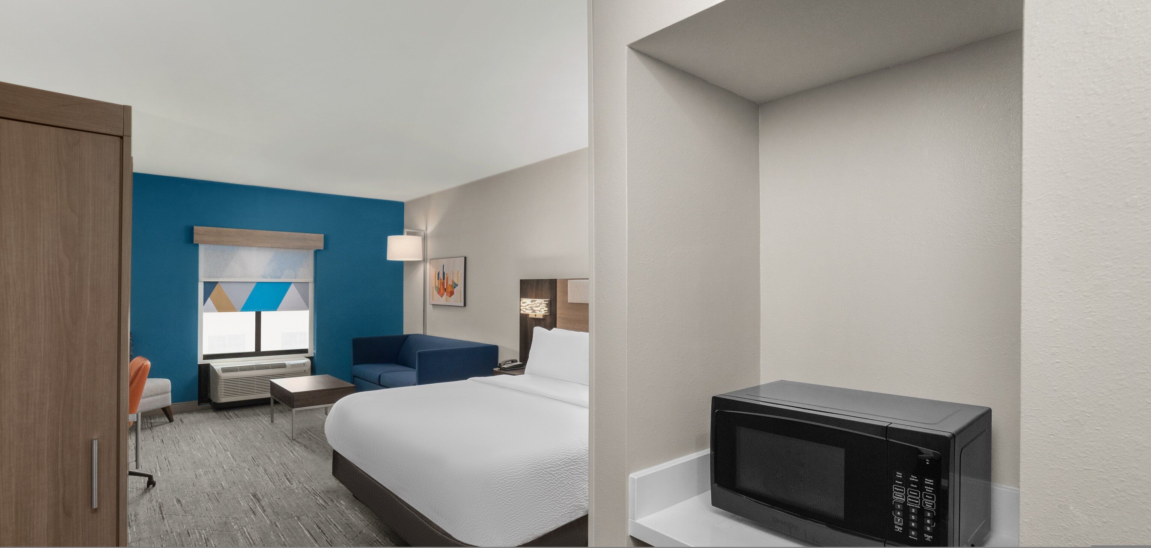 A hotel room with a bed, a desk, a chair, a microwave, and a window with a view.