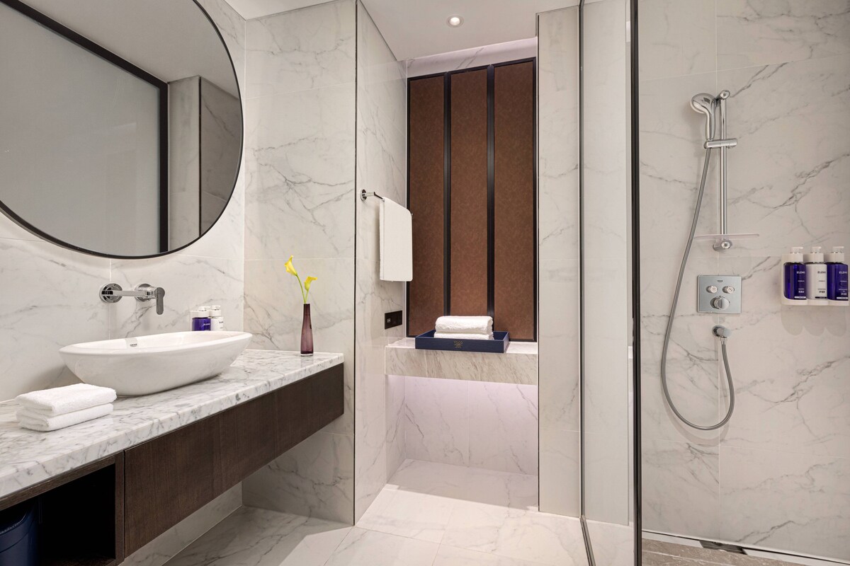 A modern bathroom with a large mirror, a sink, a shower, and a towel rack.