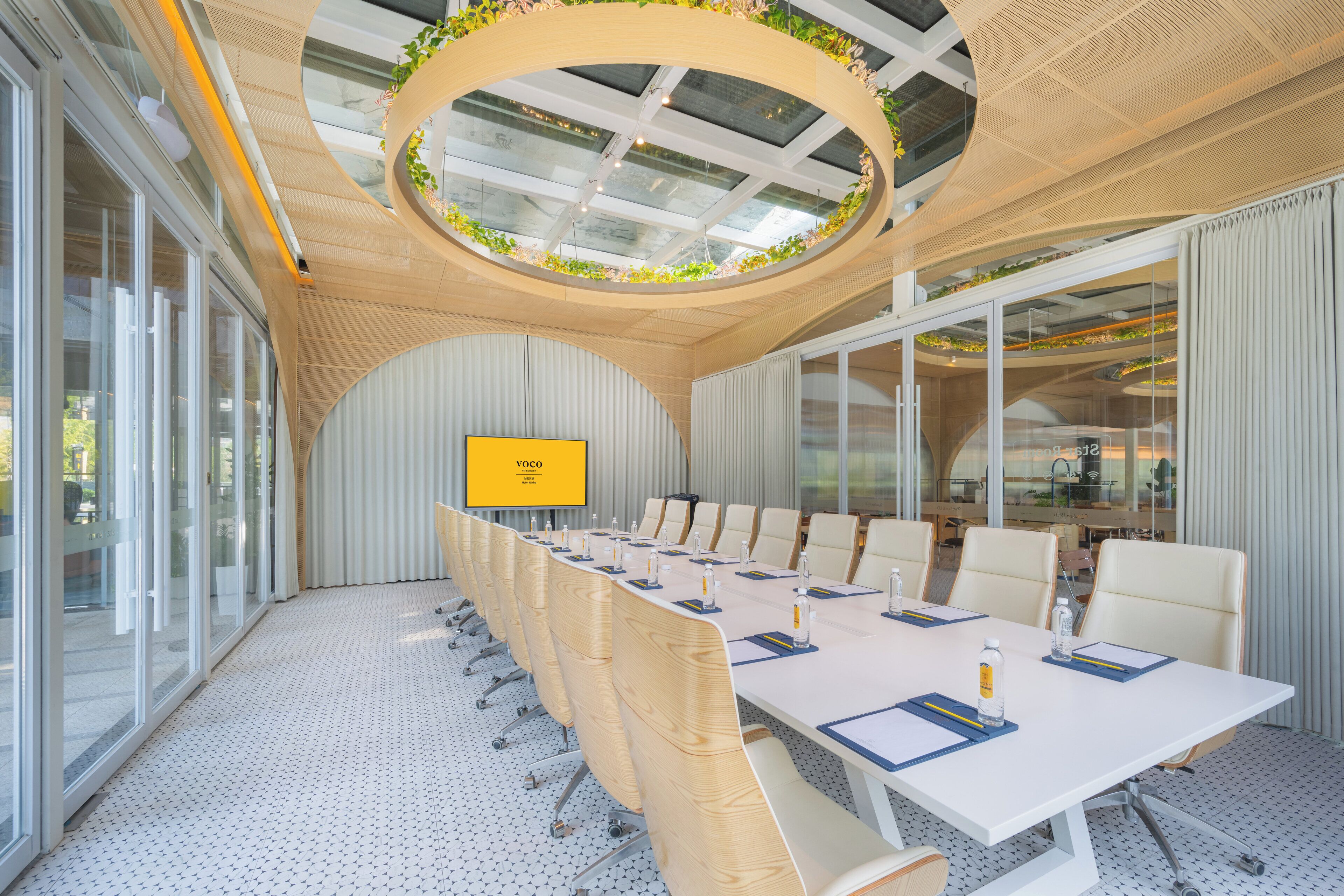 Un salón de conferencias con una mesa larga, sillas, una pantalla de televisión y un elemento decorativo circular en el techo.