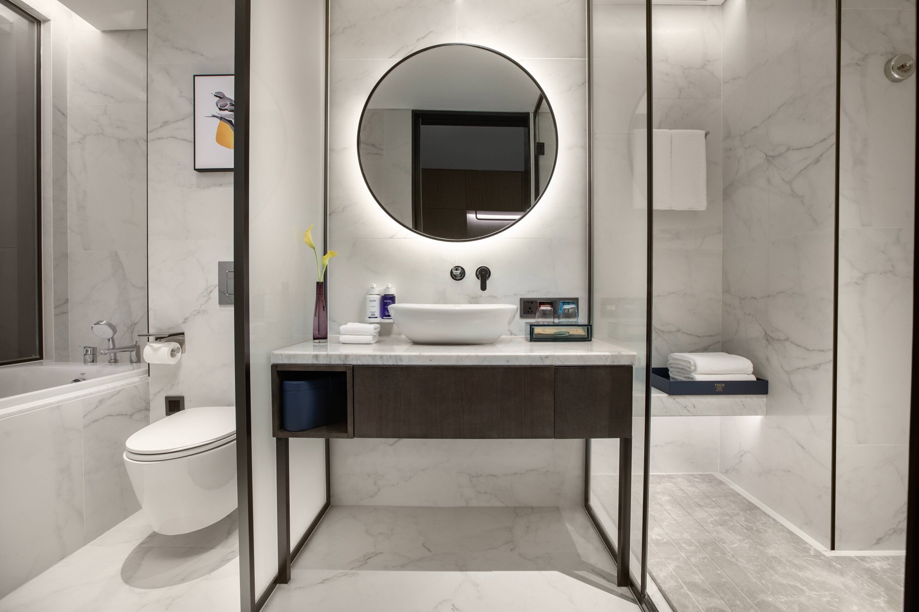 Un baño moderno con lavamanos blanco, un espejo redondo, inodoro y zona de ducha.