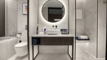 Un baño moderno con lavamanos blanco, un espejo redondo, inodoro y zona de ducha.