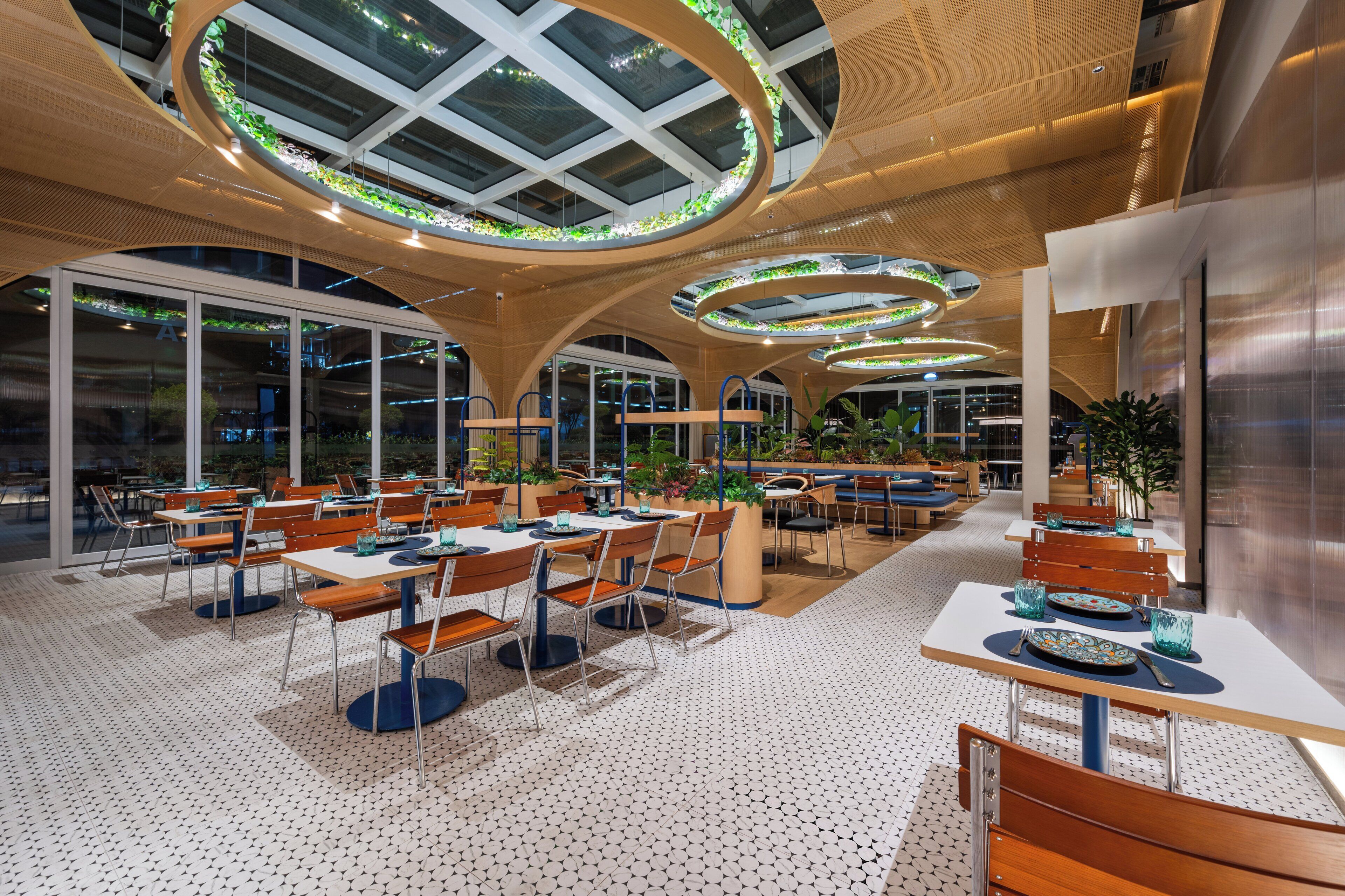 Un restaurante moderno con techos altos, tragaluces circulares y una mezcla de mobiliario de madera y metal.