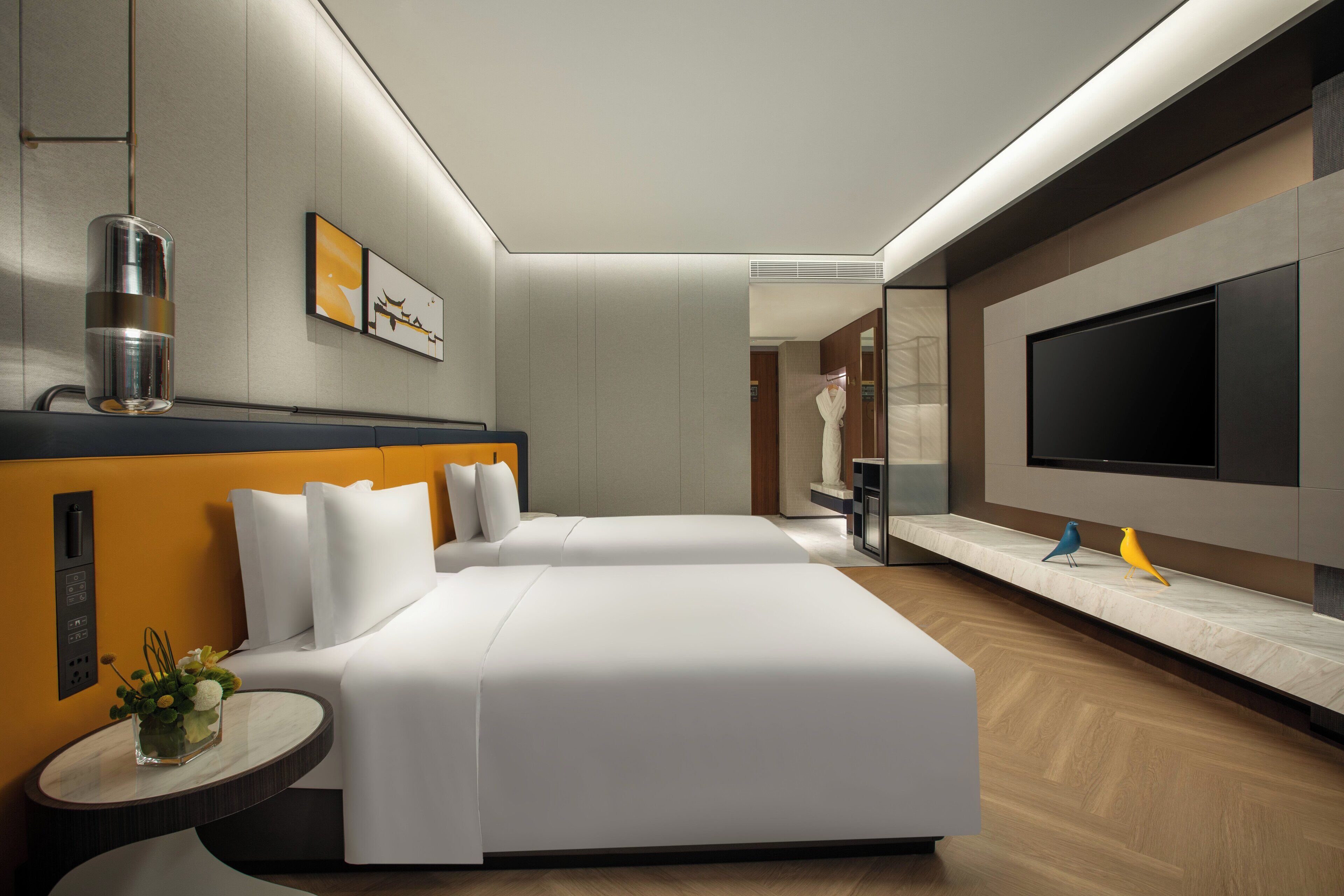 Una habitación de hotel moderna con una cama grande, un televisor de pantalla plana, una mesita con un florero y un espejo.