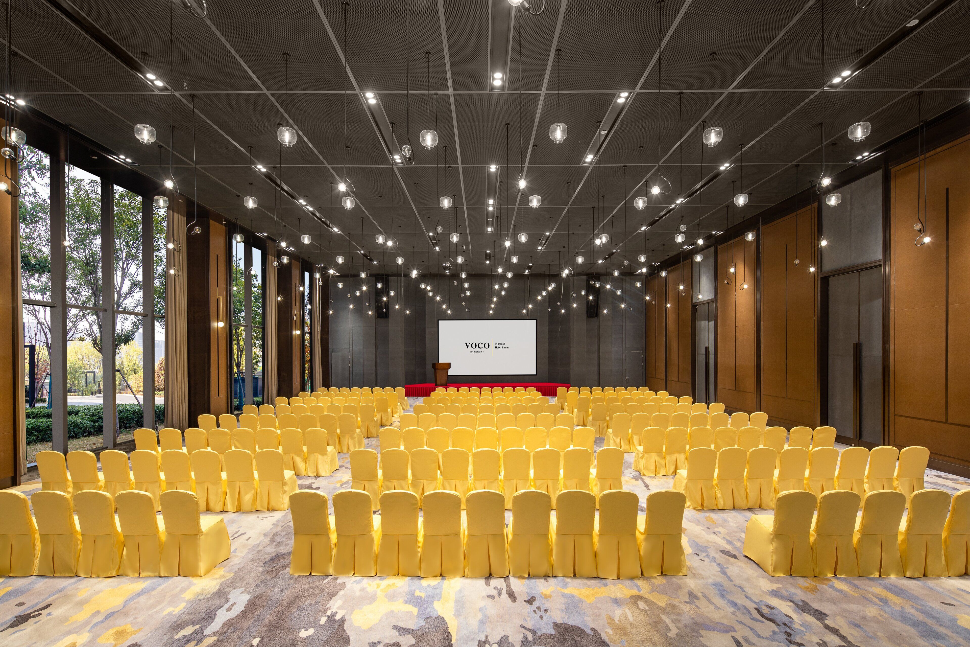 A conference room with rows of yellow chairs, a stage with a podium, and a large screen displaying "YOCO".