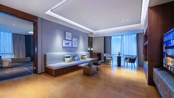 Una habitación de hotel moderna con un sofá grande, una mesa de centro, un comedor y un televisor.