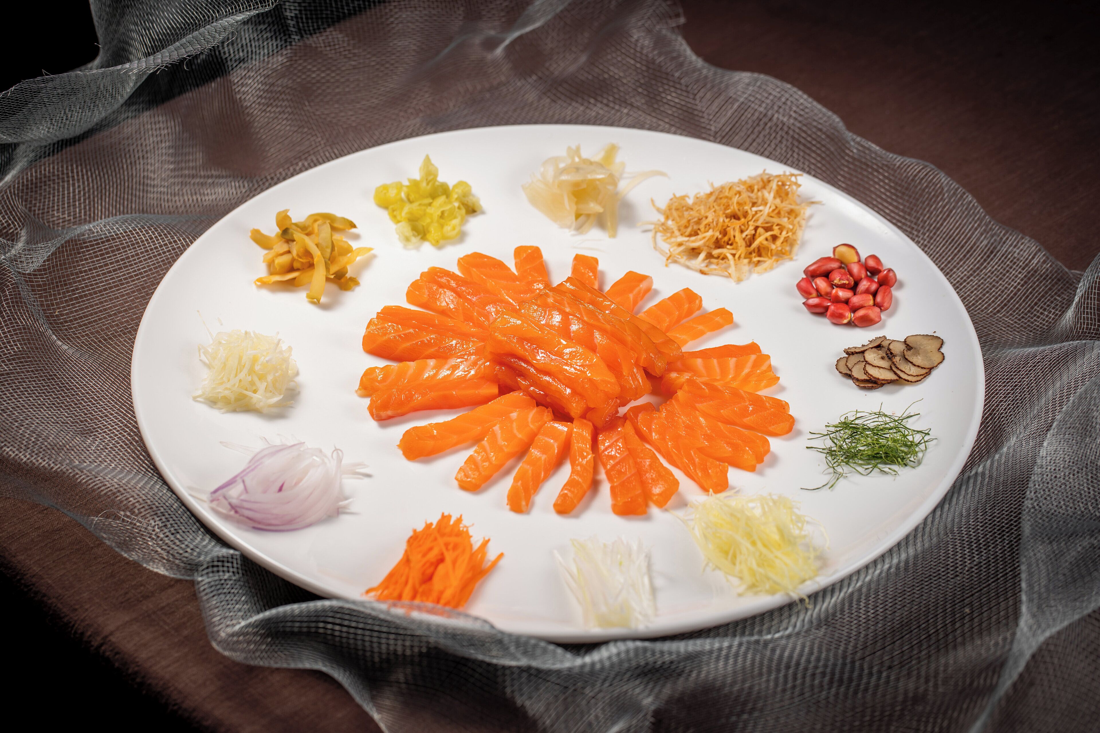 A white plate with various sliced vegetables and herbs arranged on a dark cloth.