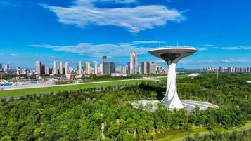 Una estructura de torre moderna en un parque urbano, con un horizonte urbano denso al fondo.