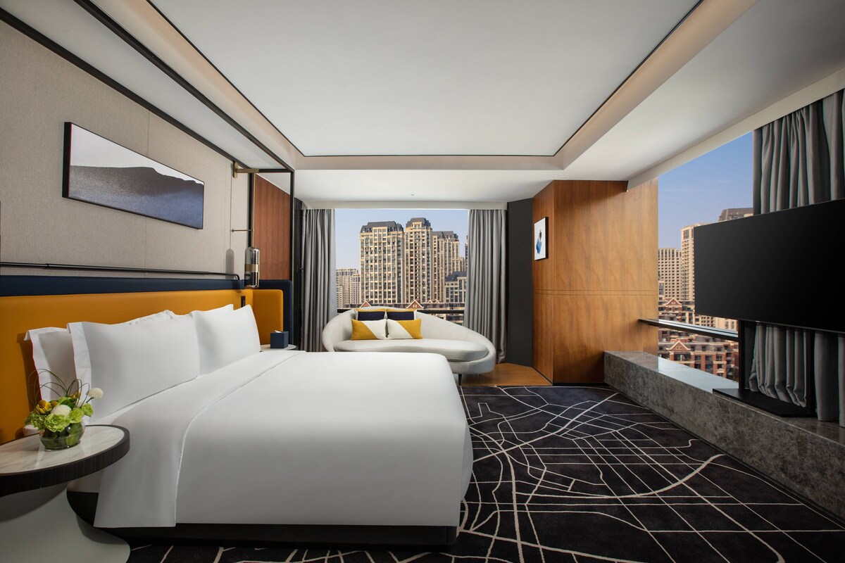 A hotel room with a large bed, a sofa, a TV, and a city view.