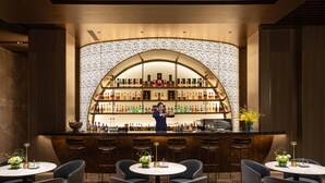 A bar area with a bartender, multiple seating tables, and a wall of liquor bottles. - voco Hefei Binhu by IHG (Hefei)