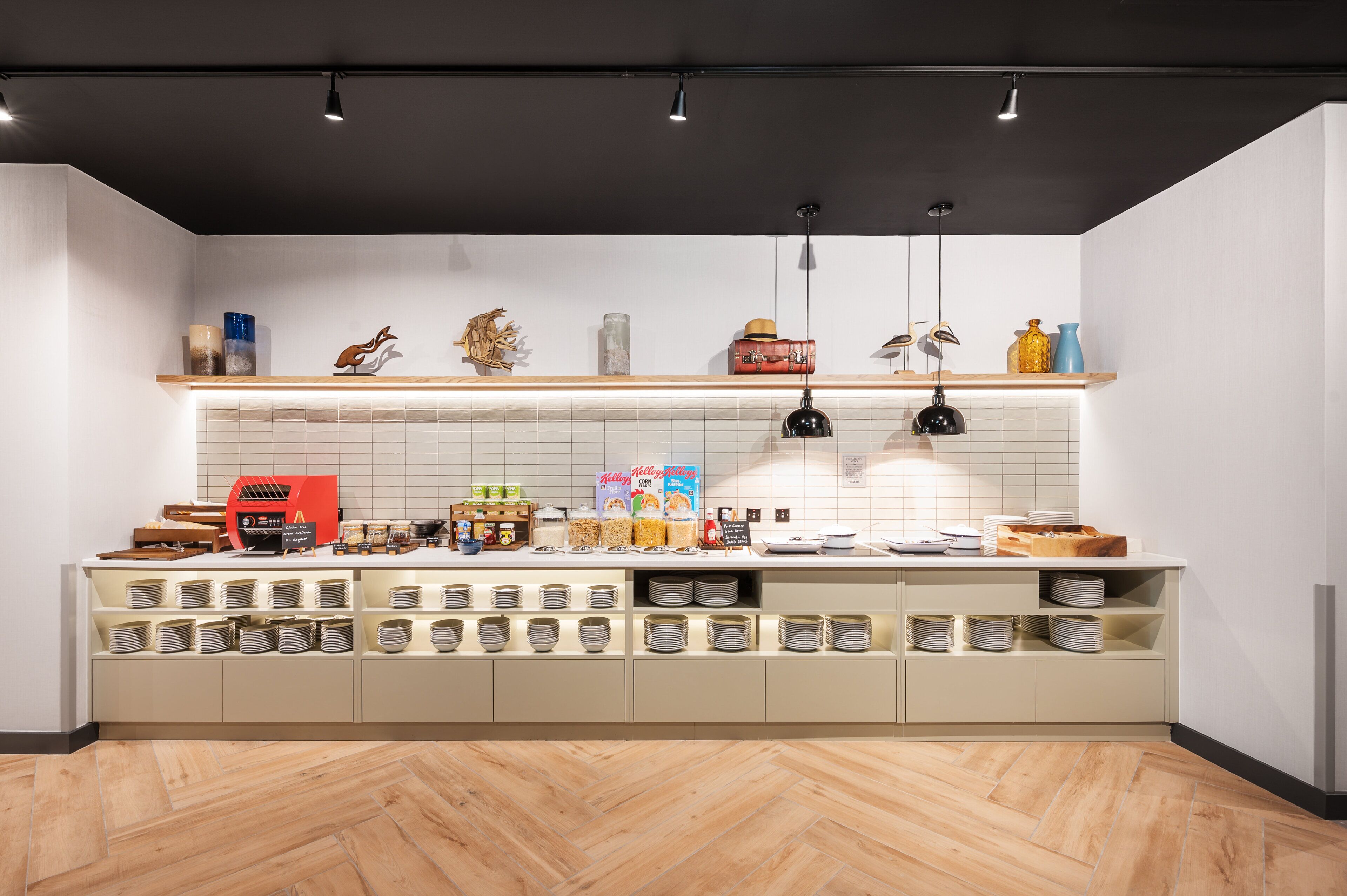 A modern kitchen with a herringbone wood floor, white tiled backsplash, and a variety of food items and kitchen appliances on the counter.