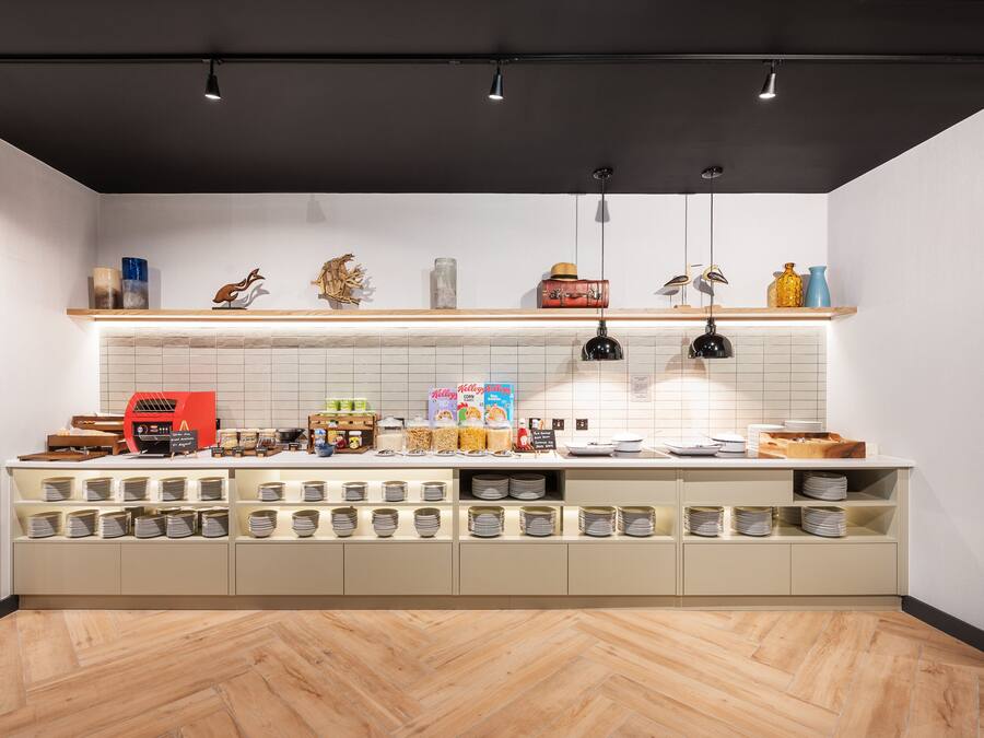 A modern kitchen with a herringbone wood floor, white tiled backsplash, and a variety of food items and kitchen appliances on the counter.