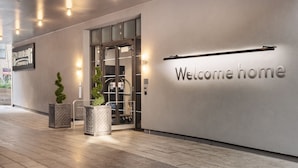 A modern hotel entrance with a 'Welcome home' sign, a glass door, and potted plants. - Staybridge Suites Brighton by IHG (Brighton)