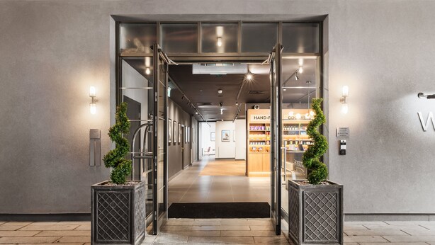 A modern hotel entrance with a glass door, a reception desk, and a visible hand sanitizer station. - Staybridge Suites Brighton by IHG (Brighton)