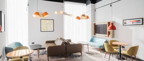 A modern lounge area with a sofa, chairs, and tables, featuring pendant lighting and artwork on the walls.
