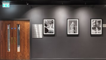 A hotel corridor with wooden doors, directional signs, and black-and-white photographs on the wall.