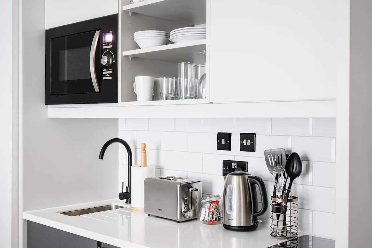 A modern kitchen with a built-in microwave, toaster, kettle, and a utensil holder.