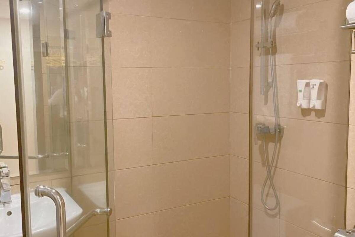 A glass-enclosed shower with a handheld showerhead and a wall-mounted control panel.