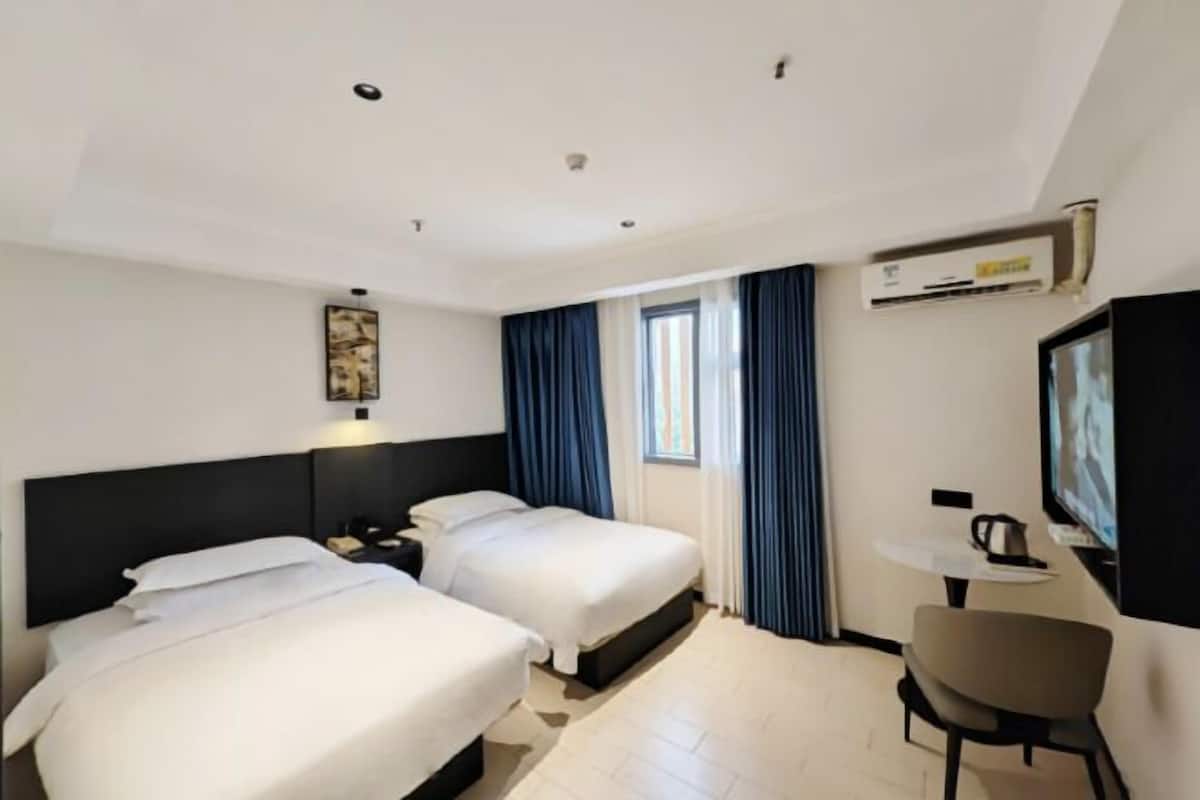 A hotel room with two beds, a desk, a chair, and a TV.