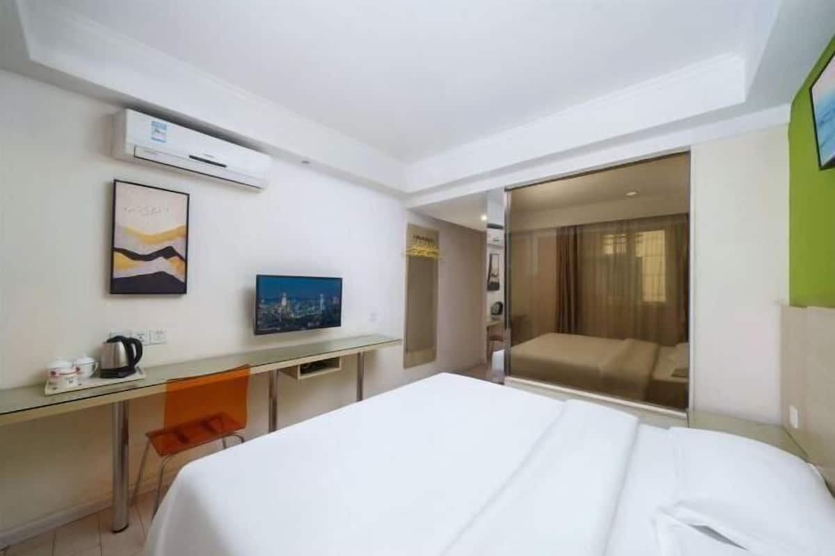 A hotel room with a bed, a desk with a chair, a television, and a sliding door leading to a balcony.