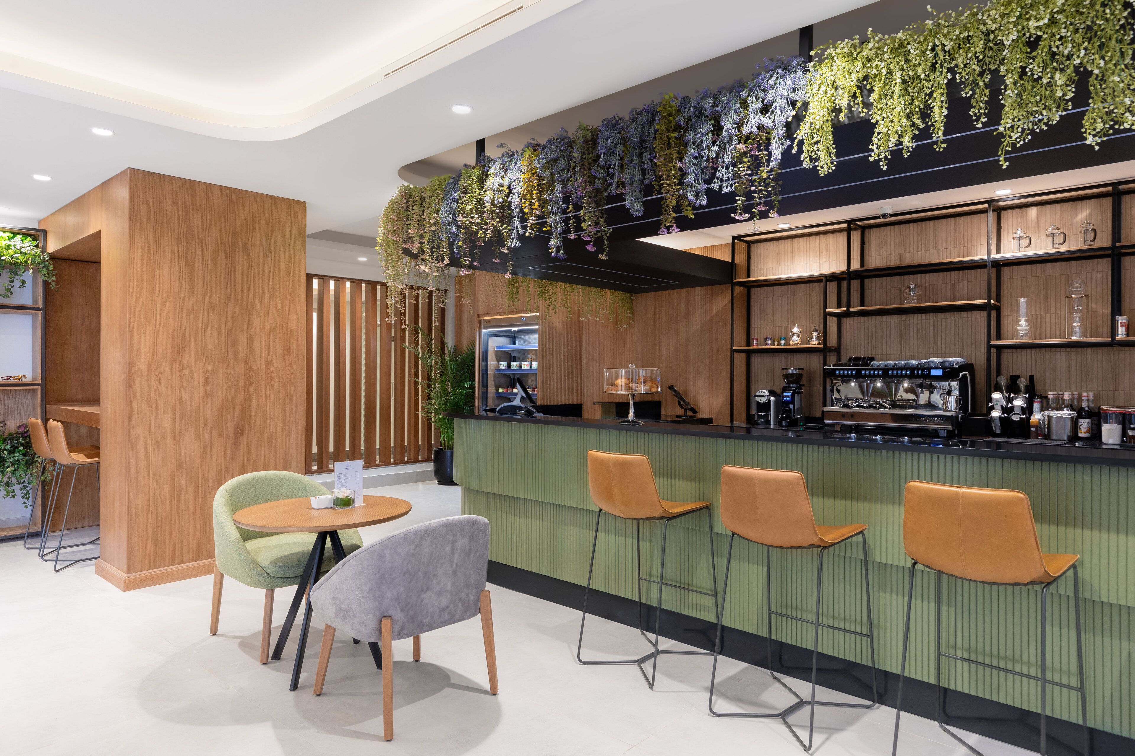 A modern bar area with wooden furniture, green bar counter, and hanging plants.