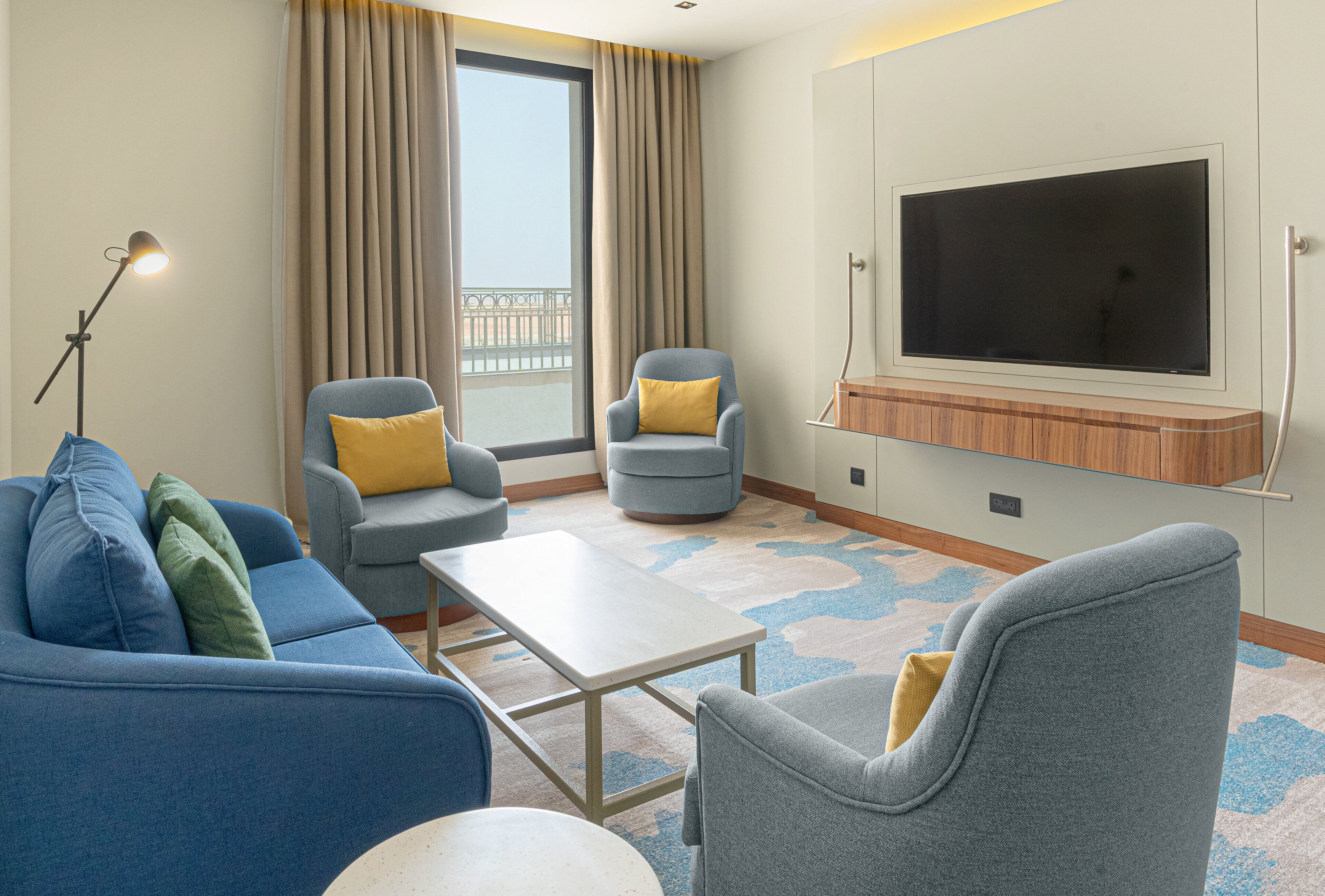 A modern living room with a sofa, two armchairs, a coffee table, and a flat-screen TV mounted on the wall.