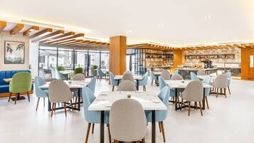 A modern restaurant with a variety of seating options including booths and tables, a bar area, and a view of the city through large windows.