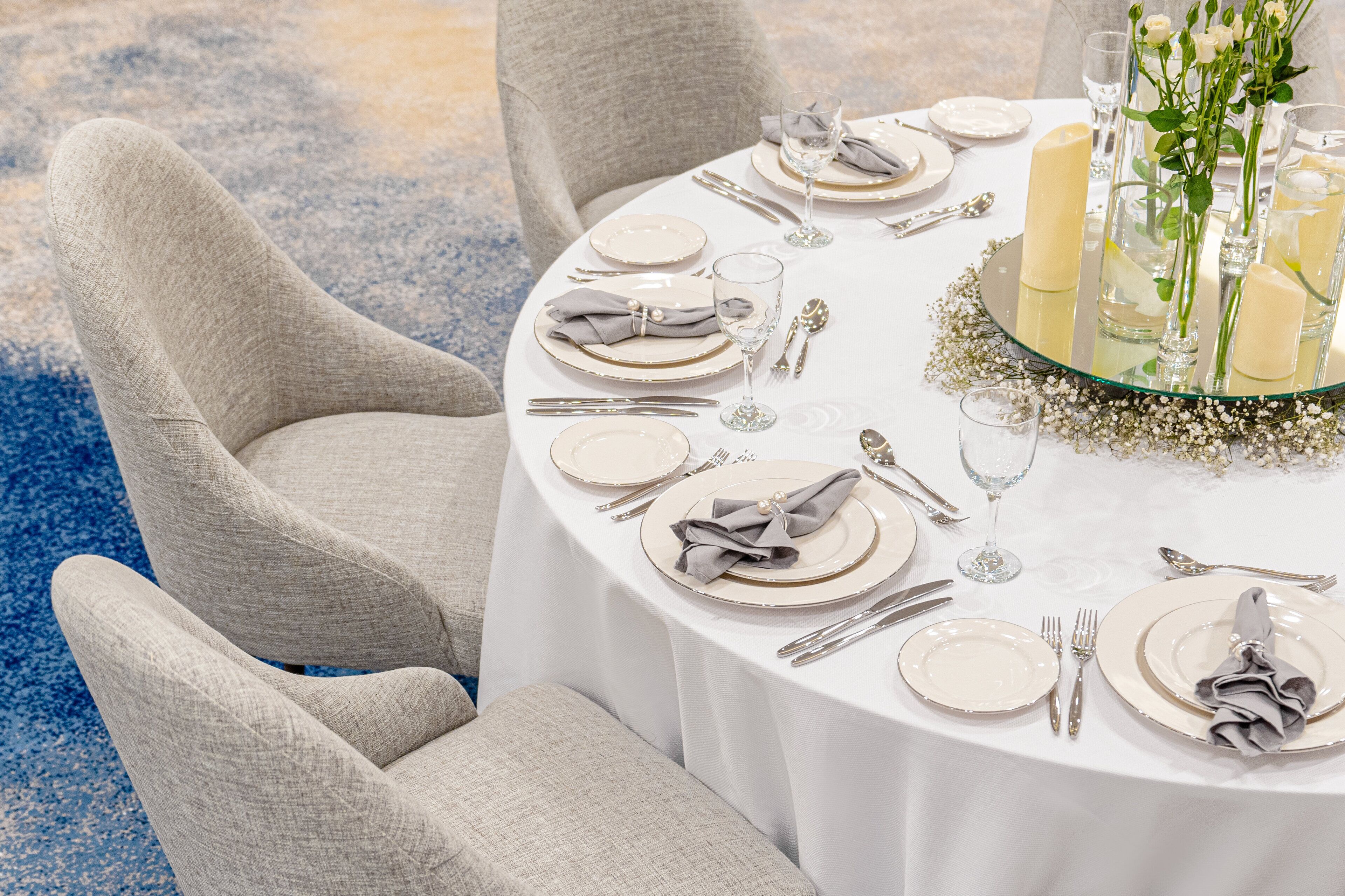 A round dining table set for four with white plates, silverware, and glasses.