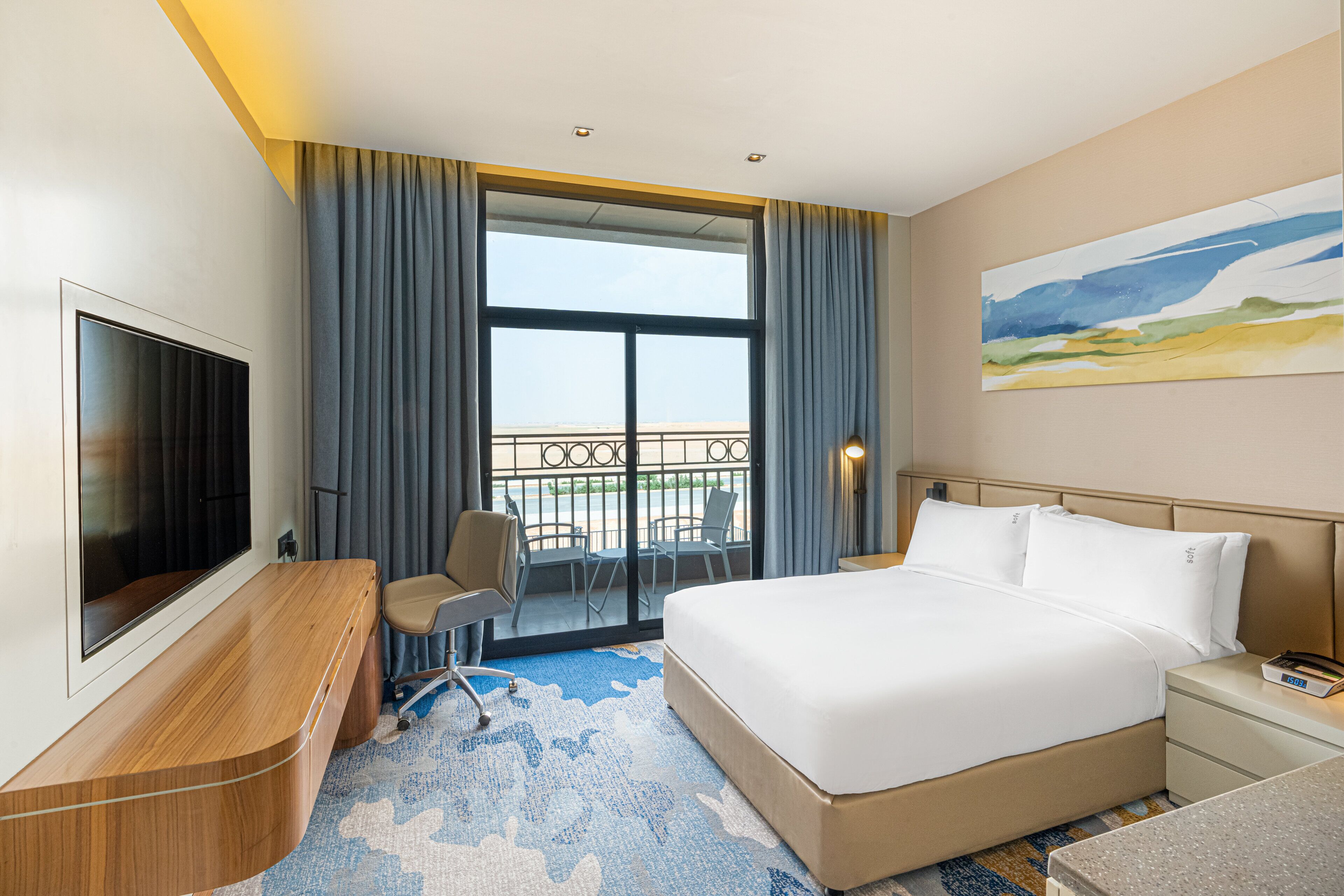 Ein Hotelzimmer mit einem großen Bett, einem Schreibtisch mit Stuhl, einem Fernseher und einem Balkon mit Blick.