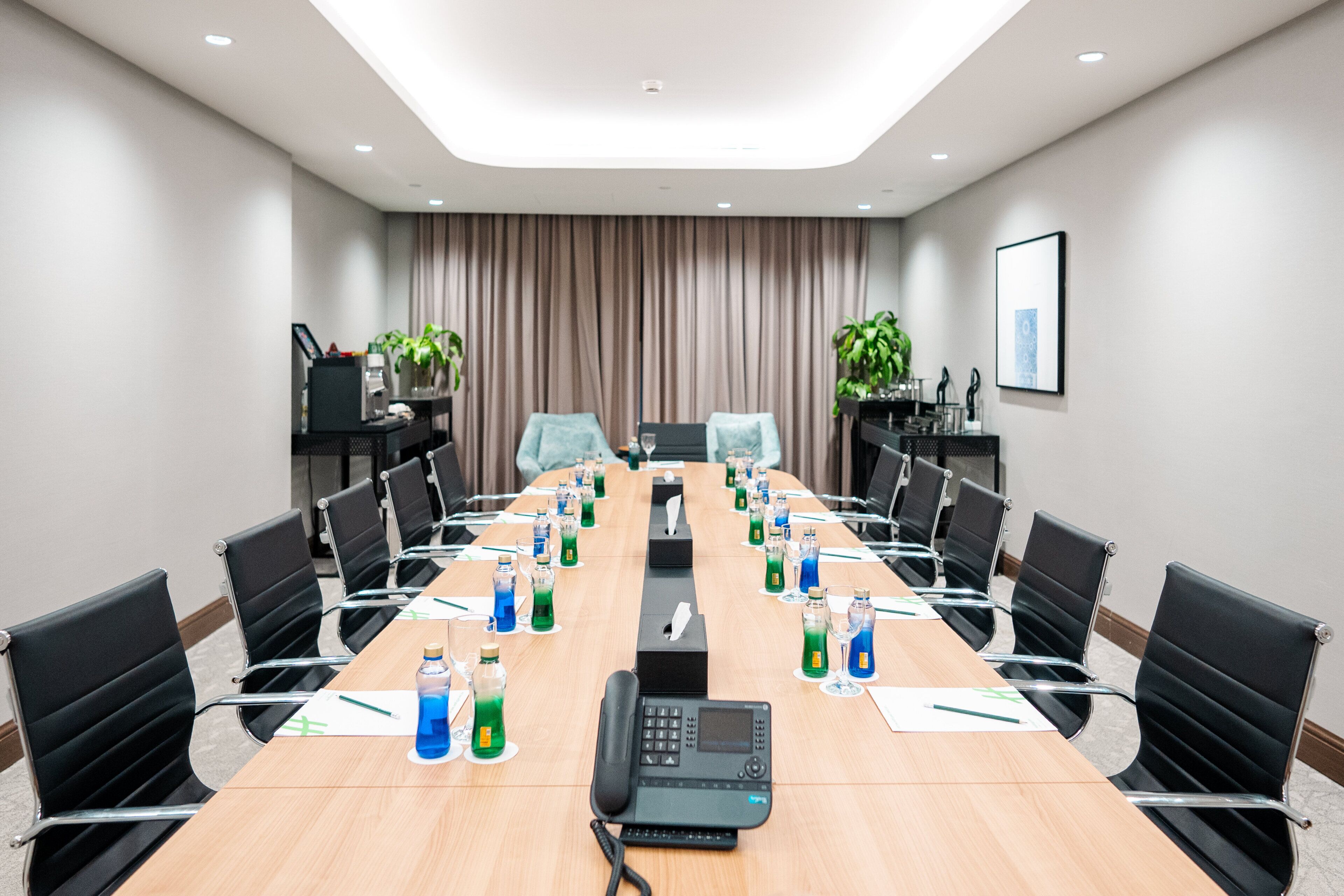 A conference room with a long table, chairs, a phone, and water bottles.