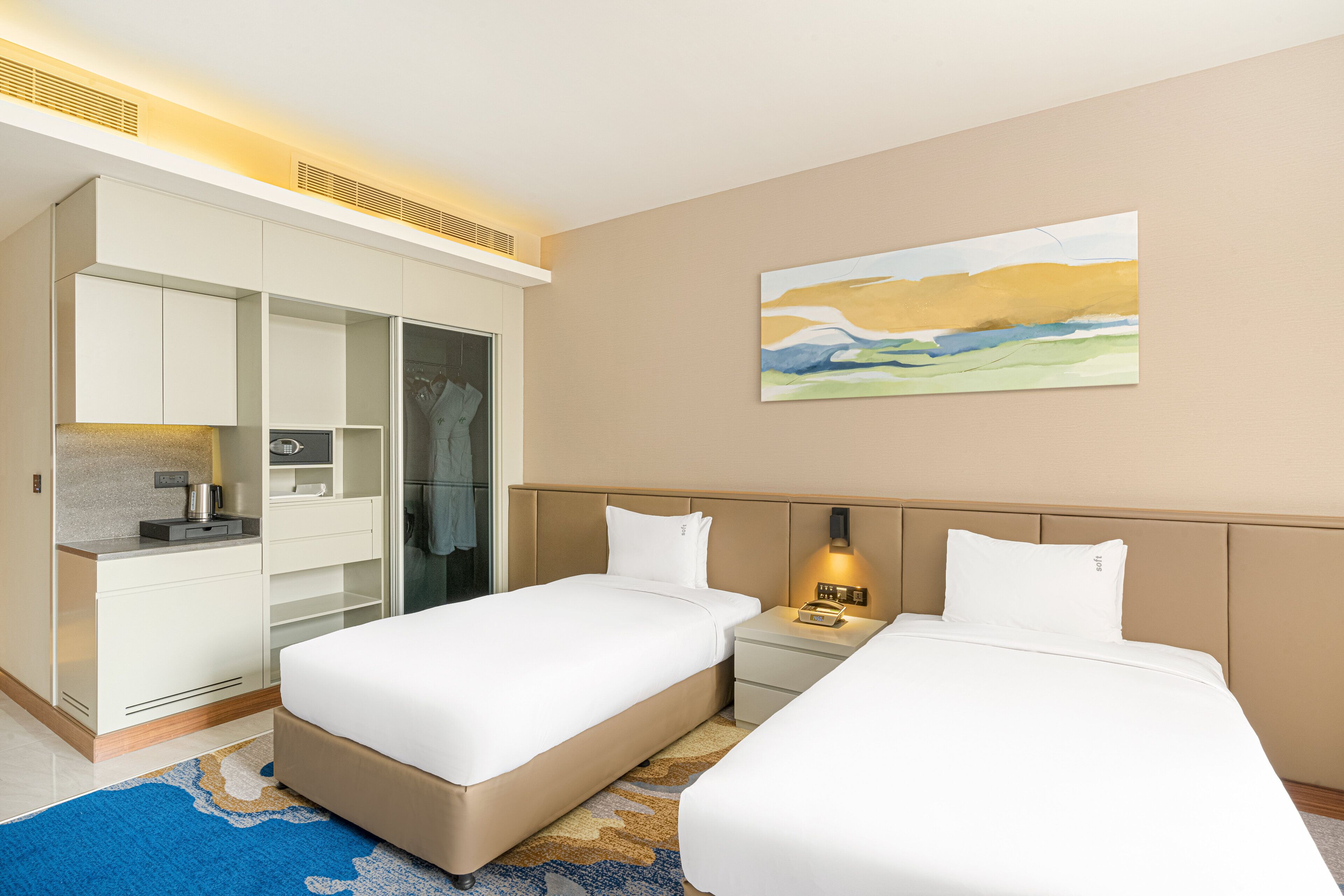 Quarto de hotel com duas camas, um guarda-roupa, uma escrivaninha e um quadro na parede.