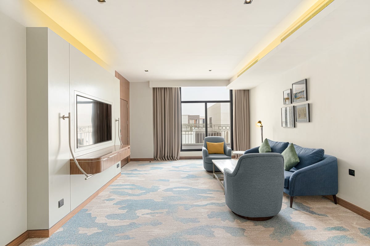 A modern hotel room with a large TV, comfortable seating, a view of the city, and a large window with curtains.