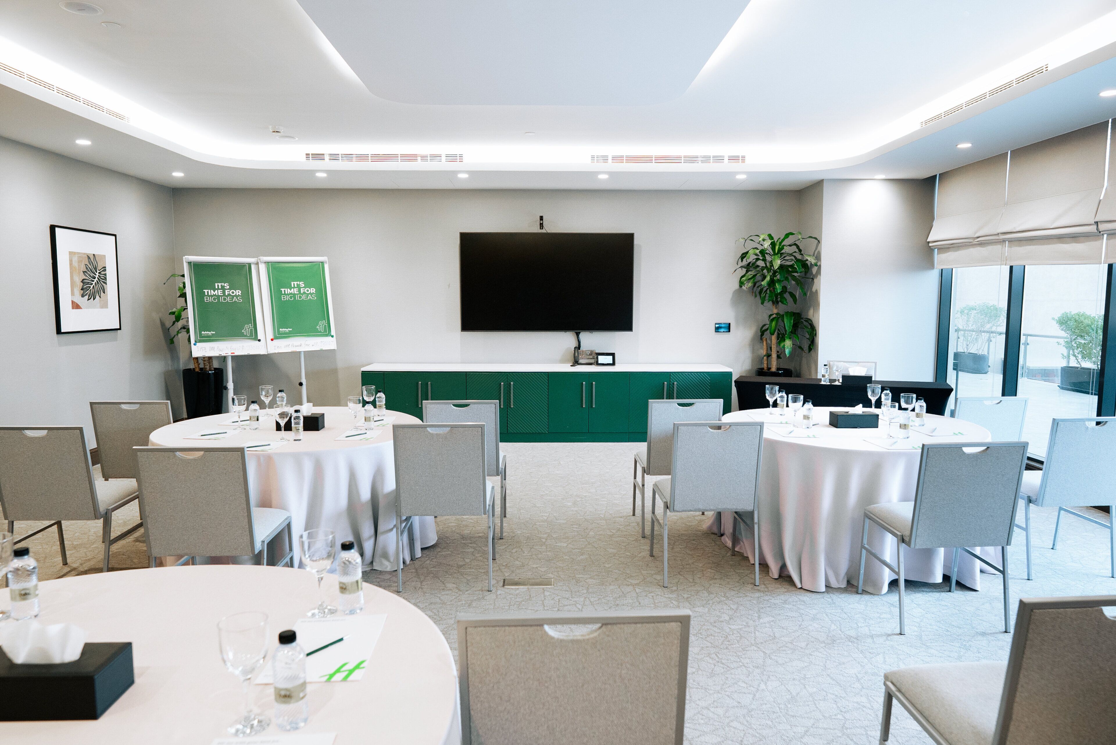 A conference room with round tables, chairs, a flat-screen TV, and green cabinets.