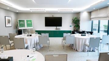 A conference room with round tables, chairs, a flat-screen TV, and green cabinets.