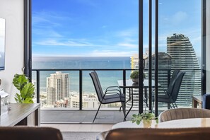 A balcony with a view of the ocean and a cityscape, featuring a table and chairs.