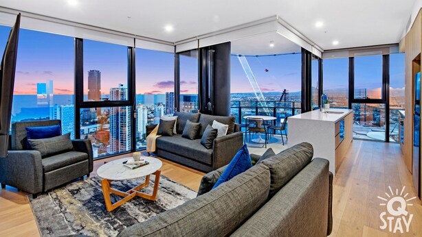 A modern living room with a city view, a sofa, a coffee table, and a dining area with a view. - Casino Private Apartments - QStay (Broadbeach)