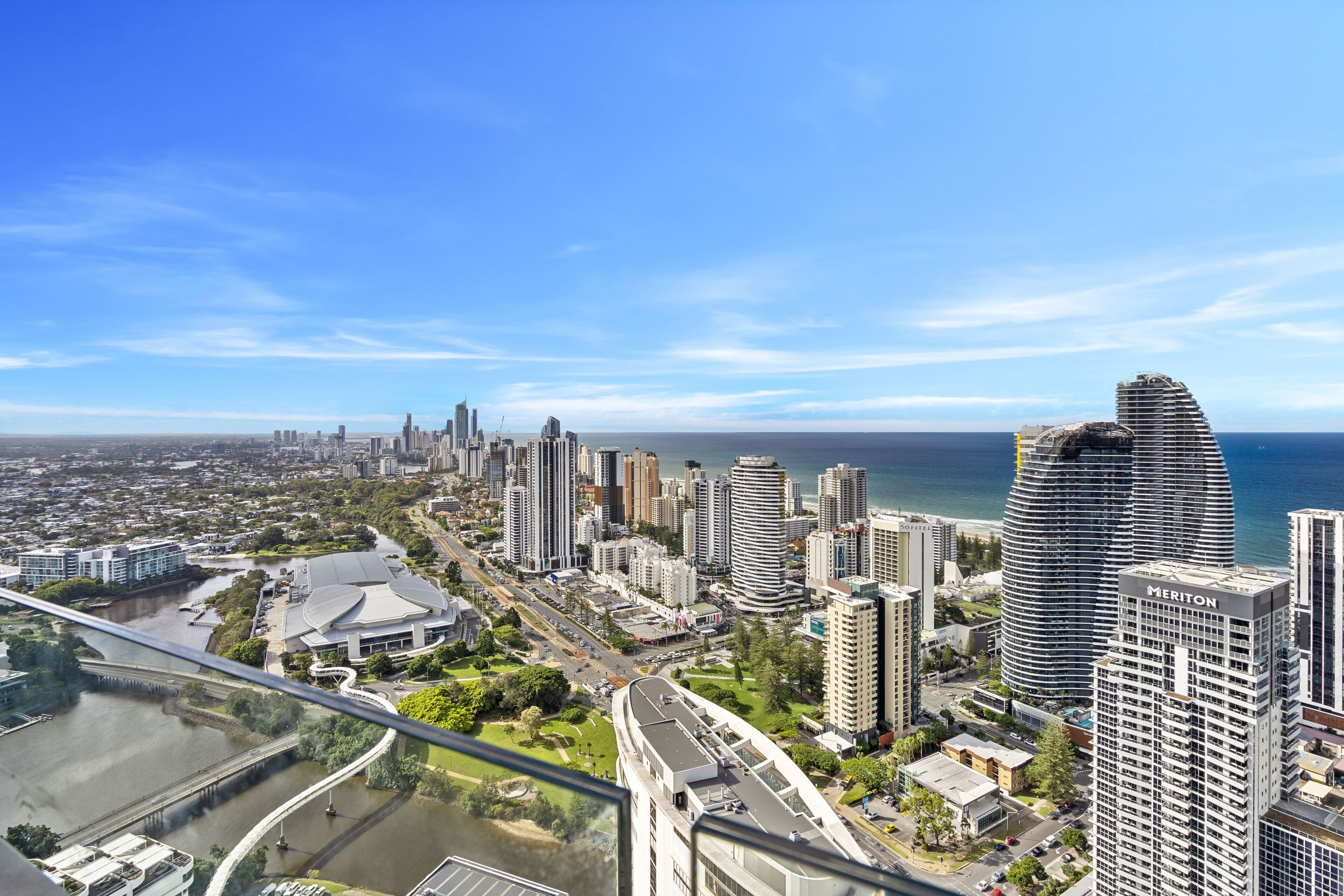 Un hotel de gran altura con fachada curva, vista al horizonte de la ciudad y un río en primer plano.