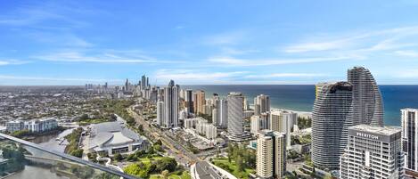 Un hotel de gran altura con fachada curva, vista al horizonte de la ciudad y un río en primer plano.