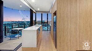 A modern kitchen with a large island, a view of the cityscape, and a balcony with a pool. - Casino Private Apartments - QStay (Broadbeach)