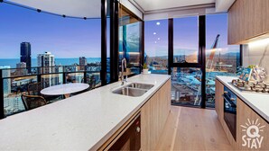 A modern kitchen with a large window, a dining area, and a view of the cityscape and ocean. - Casino Private Apartments - QStay (Broadbeach)